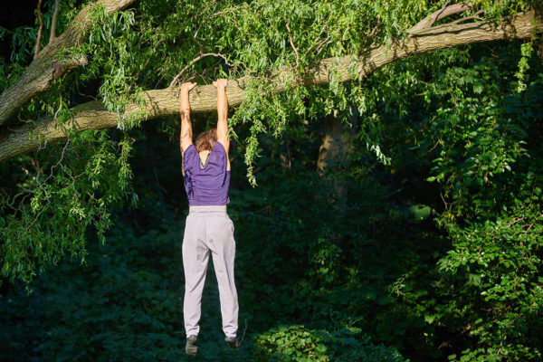 Acrobat hanging high up in the air from a tree branch