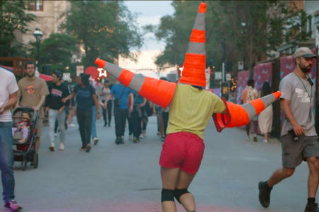 Acrobat wobbling down the street with traffic cones on her head